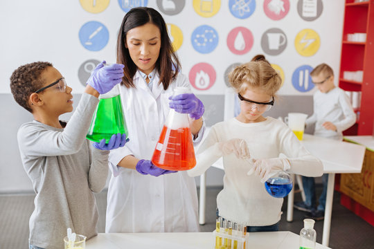 Fair assessment. Pleasant young teacher holding a flask and checking the result of her students chemical experiment while the boy asking her advice about his experiment