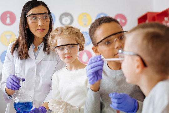 Be careful. Pleasant chemistry teacher looking at her students with a worried expression while they mixing chemicals in a wrong way