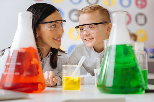 Smart ideas. The close up of a pleasant upbeat chemistry teacher and her student discussing the chemical reaction while watching it going on in the flask standing on the table