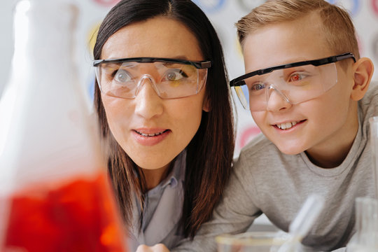 Fascinated by result. The close up of a cheerful young chemistry teacher and her student leaning closer to the table and observing the reaction in the flask