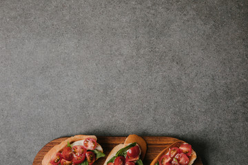 top view of delicious italian bruschetta on wooden board on grey background