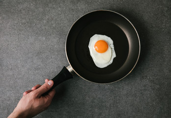 partial top view of person holding frying pan with fried egg on grey
