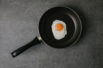 top view of frying pan with tasty fried egg on grey