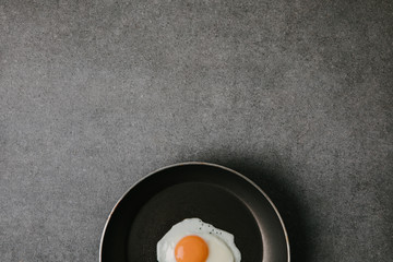 top view of frying pan with tasty fried egg on grey background