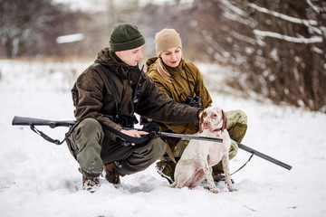 two hunters with rifles in a snowy winter forest.