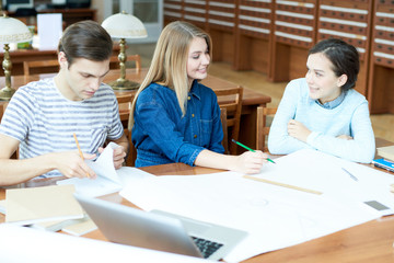 Obraz premium Group of positive optimistic friends drawing sketch together discussing classes in library after university and sitting at table with blueprint