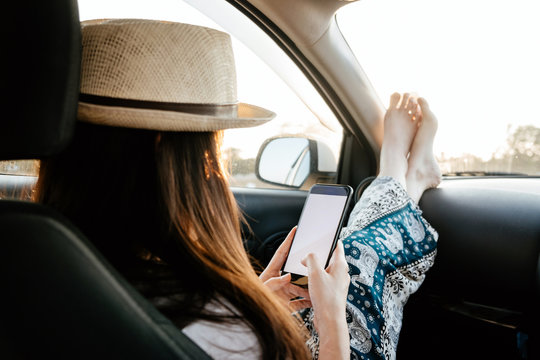 Young Woman Traveler Using Phone On Car In Sunset Light.