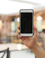 Hand of businessman holding a smartphone in empty black screen on Restaurant blur background.