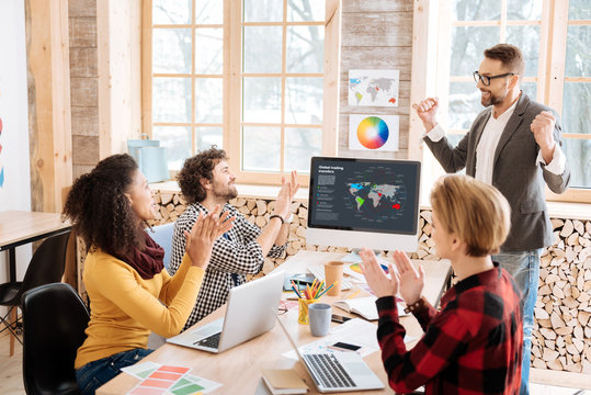 Great results. Good-looking exuberant smiling and standing in front of his employees and they clapping to him
