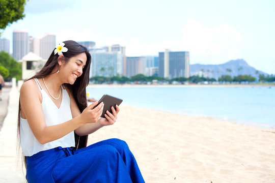 Biracial teen girl on beach using tablet computer, Waikiki, Honolulu