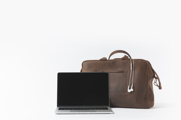 close up view of laptop with blank screen and stylish bag with earphones isolated on white