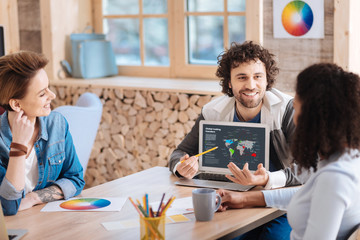 Talking about results. Handsome cheerful curly-haired man smiling and showing information on his...