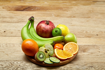 Ripe fresh fruits in a wooden plate on a light wooden background, selective focus, close-up, top view