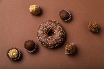 Chocolate donuts with chocolate truffles on brown background. Monochromatic concept.