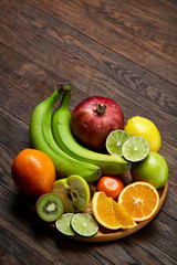 Ripe fresh fruits in a wooden plate on a light wooden background, selective focus, close-up, top view