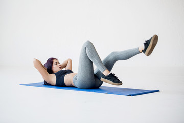 Sport tutorials for beginners to warm up. The attractive athletic trainer is lying on the mat and doing bicycle crunches in the white studio.