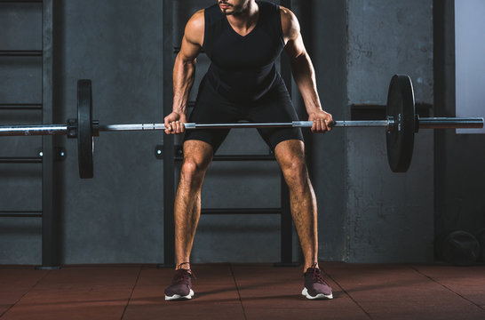 Cropped image of athlete holding barbell in sports hall