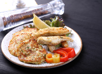 Fried fish with zuccini pancakes on a plate