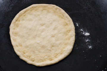 Preparation of homemade pizza. Cooking process. Pull out the dough. Top view on dark metallic background.