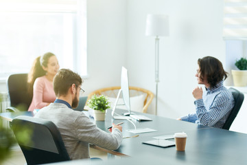 Group of confident ambitious young startuppers discussing business development and brainstorming in meeting room, bearded man summarizing main ideas