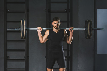 Young sportsman holding barbell on shoulders in gym