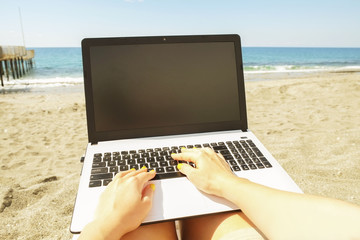 First person view. Female blogger hands close up, typing on laptop computer blank screen, keyboard, writing blog entry. Young woman programmer coding, notebook at sea beach. Perks of freelance concept