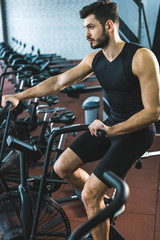 Fototapeta na wymiar Young sportsman doing workout on exercise bike in sports center