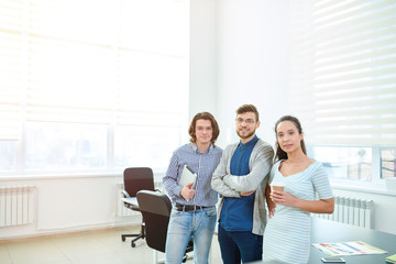 Fototapeta premium Content confident young multiethnic business colleagues in casual clothing looking at camera and standing by table in board room