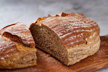 Fresh rye bread loaf on a wooden chopping board over white textured background, shallow depth of field