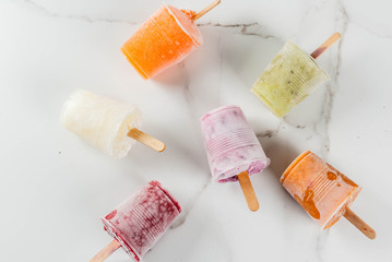 Healthy summer desserts. Ice cream popsicles. Frozen tropical juices, smoothies blueberries. currants, orange, mango, kiwi, banana, coconut, raspberry. On white marble table copy space top view