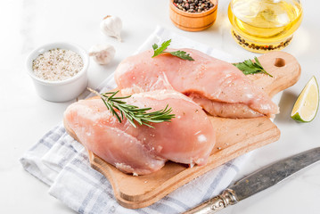 Raw meat, chicken breast filet, with olive oil, herbs and spices on white marble background, copy space