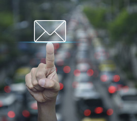 Hand pressing mail flat icon over blur of rush hour with cars and road, Contact us concept