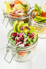 Fresh salads in jar with fresh vegetables and healthy dressings,  on white marble table, copy space