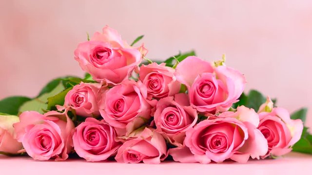 Woman placing pink roses on pink wood table, Mother's Day background closeup.