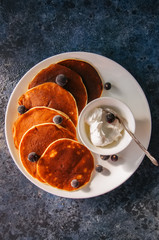Cottage cheese pancakes with sour cream and berries on a white plate on a blue stone background.