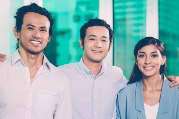 Closeup of three smiling middle-aged business people standing, looking at camera and embracing. Front view.