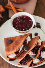 Chocolate crepes (blinis) with sour cream and black currant sauce on a white plate. Wooden...