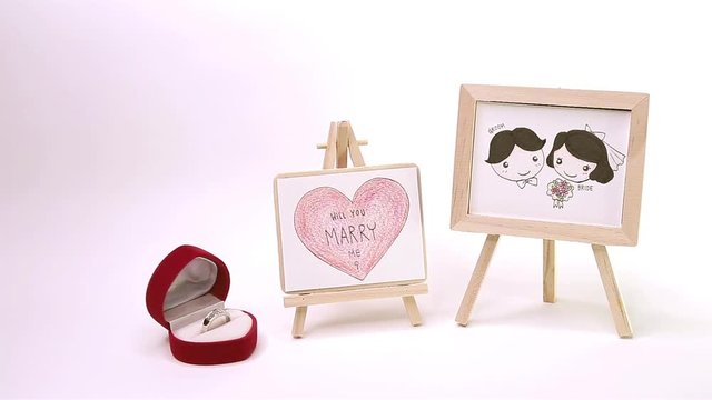 Surprise With Ring, Lovely Groom and Bride and Big Heart write ' Will You Marry Me ? ' Drawing by Color Pencil on Wooden Frame in White Background 