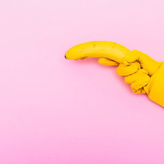 hand in yellow glove is holding a banana like a gun on a pink background
