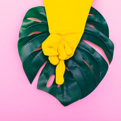 Fototapeta na wymiar a hand in a yellow glove depicts an aggressive gesture of fuck you on pink background with palm. minimalism and surrealism