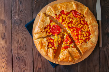 Tomato and sweet corn galette on a wooden board. Top view. Wooden background.