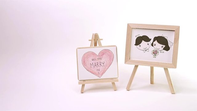 Lovely Groom and Bride and Big Heart write ' Will You Marry Me ? ' Drawing by Color Pencil on Wooden Frame in White Background 