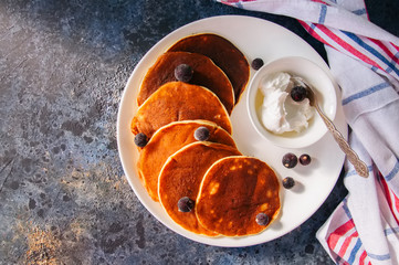 Cottage cheese pancakes with sour cream and berries on a white plate on a blue stone background.