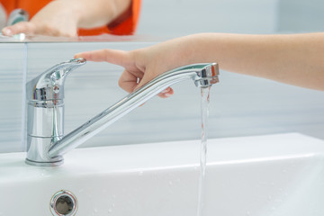 The child's hand closes the water from the mixer by pressing the finger on the handle