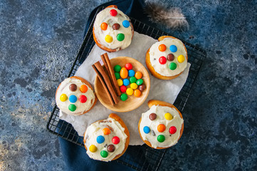 Classic cinnamon rolls - cinnabons with cream cheese frosting with smarties. Blue stone background. Top view.