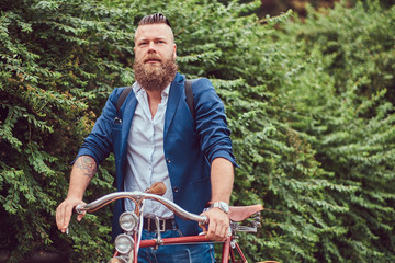 Male dressed in casual clothes, standing with a retro bicycle in a park.