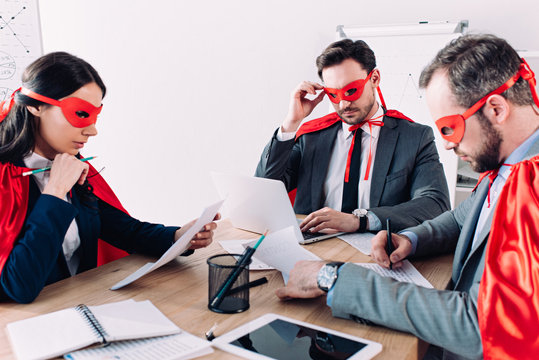 pensive super businesspeople in masks and capes working in office
