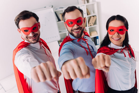 super businesspeople in masks and capes showing fists in office