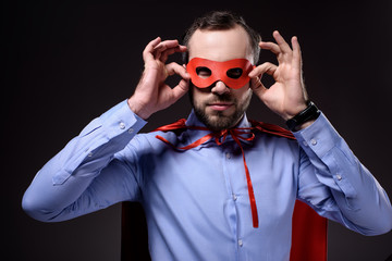 handsome super businessman in cape holding mask isolated on black