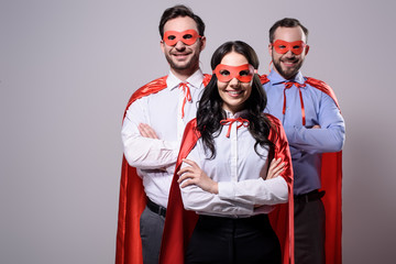 smiling super businesspeople in masks and capes with crossed arms isolated on grey